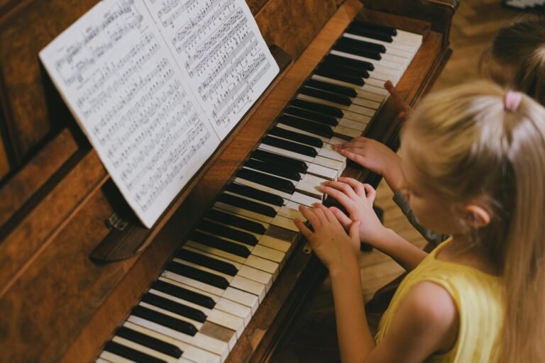 A young girl with blond hair playing piano, following music sheets indoors.