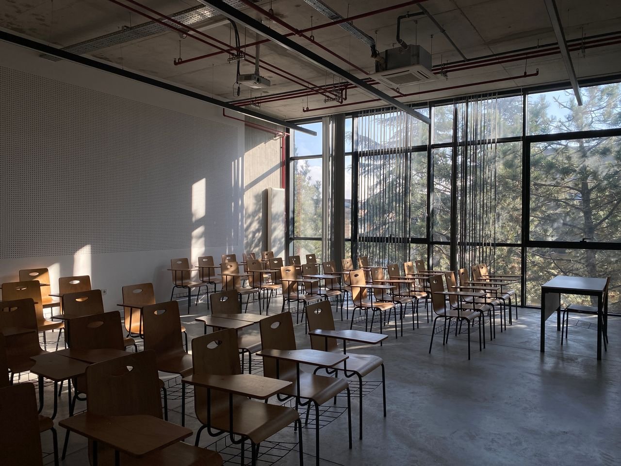Sunlit empty classroom in Ankara, Türkiye, featuring rows of wooden chairs and desks by a large window.
